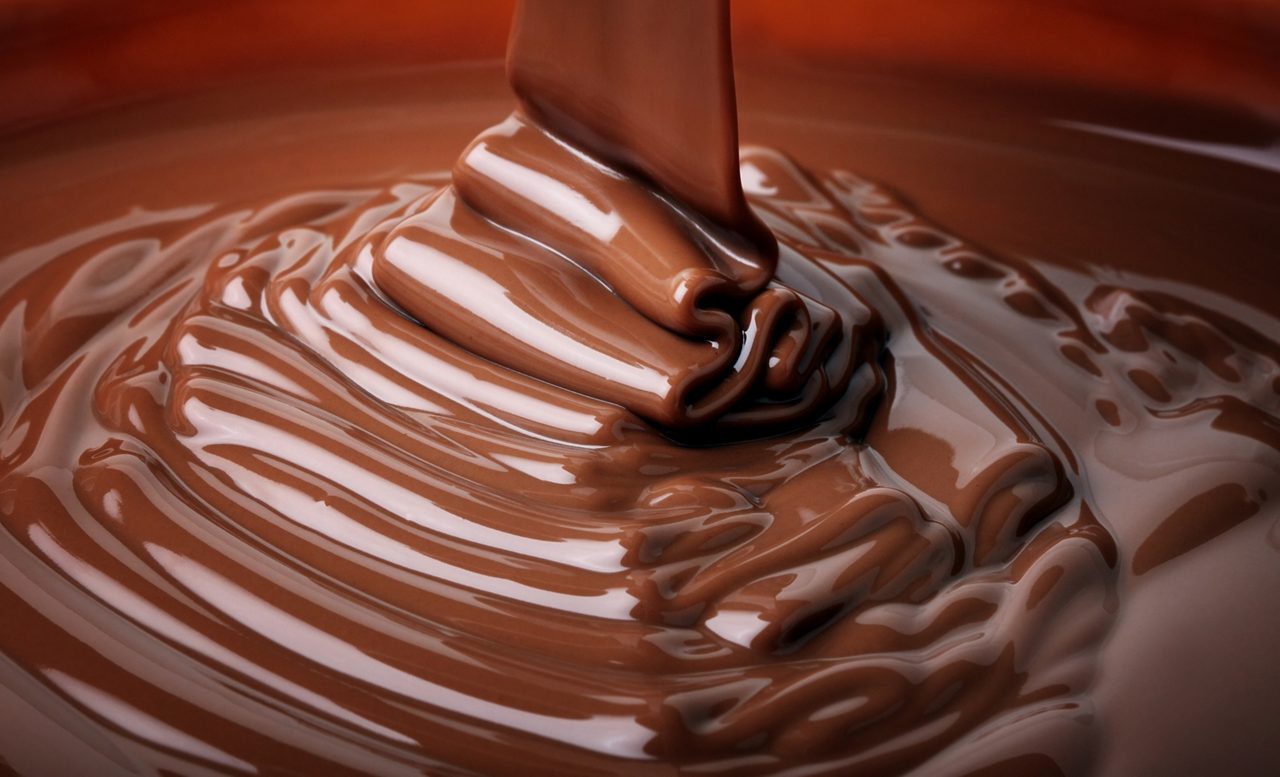 Close-up of thick melted chocolate being poured, forming smooth ripples and glossy folds on a chocolate surface.