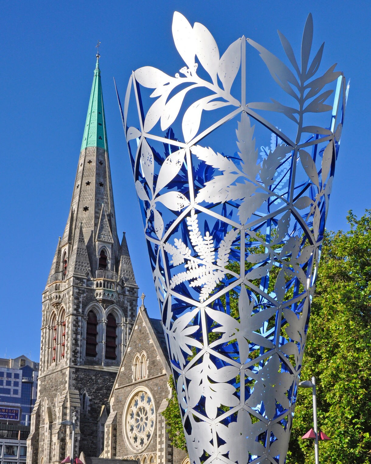 View of Christchurch Cathedral’s stone spire beside the silver and blue Chalice sculpture under a clear blue sky.