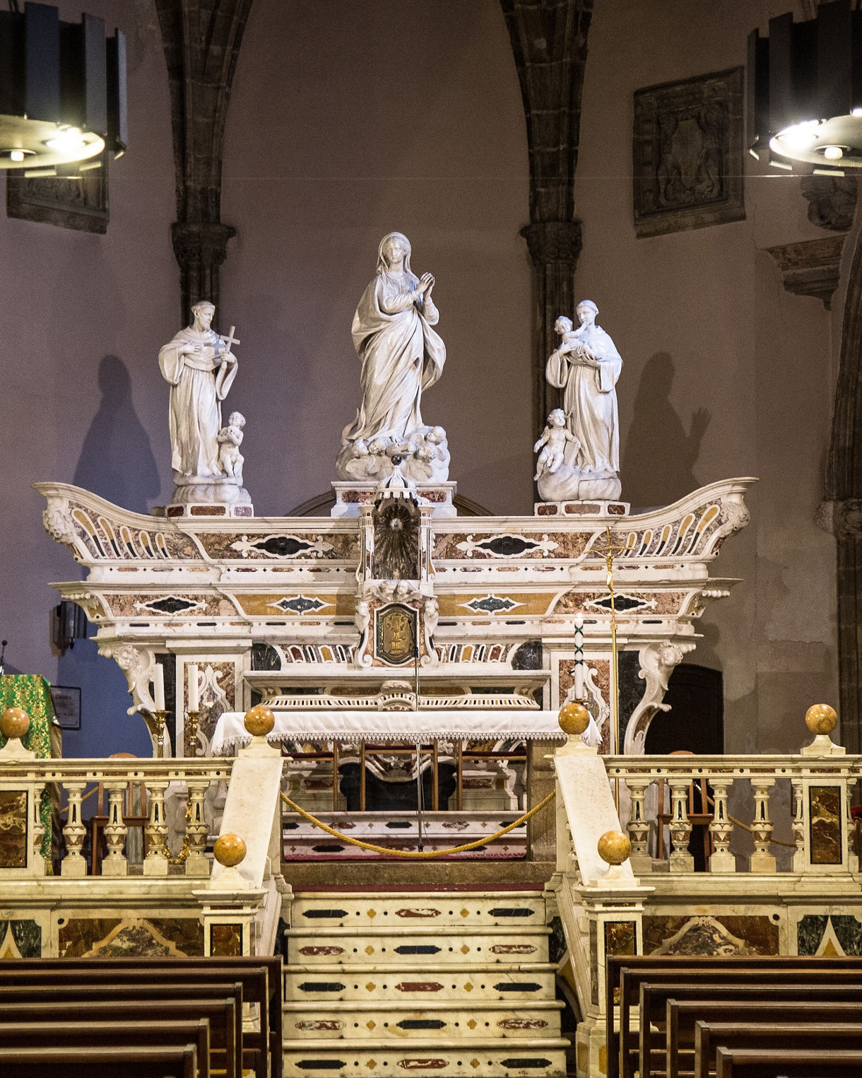 Intricately carved marble altar with statues inside a stone church, viewed from the pews.