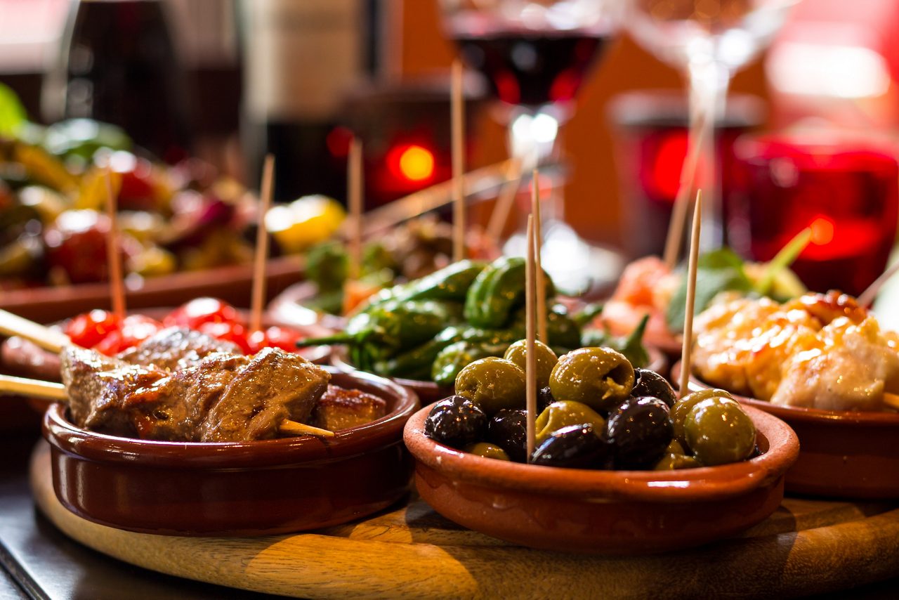 Assorted spanish tapas in terracotta bowls including marinated olives and grilled meat skewers.