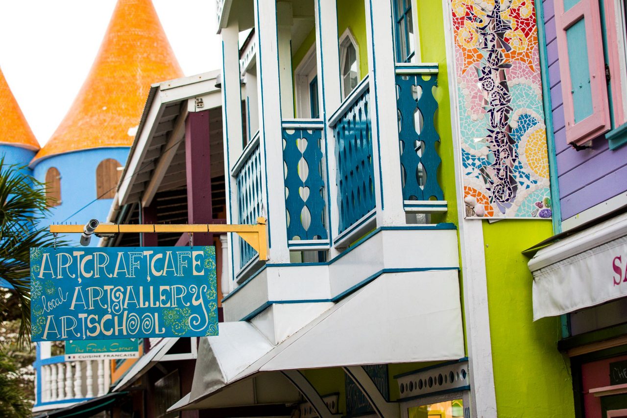Colorful Caribbean colonial buildings with bright lime green, blue, and pink facades featuring decorative balconies and an "Art Craft Cafe" sign