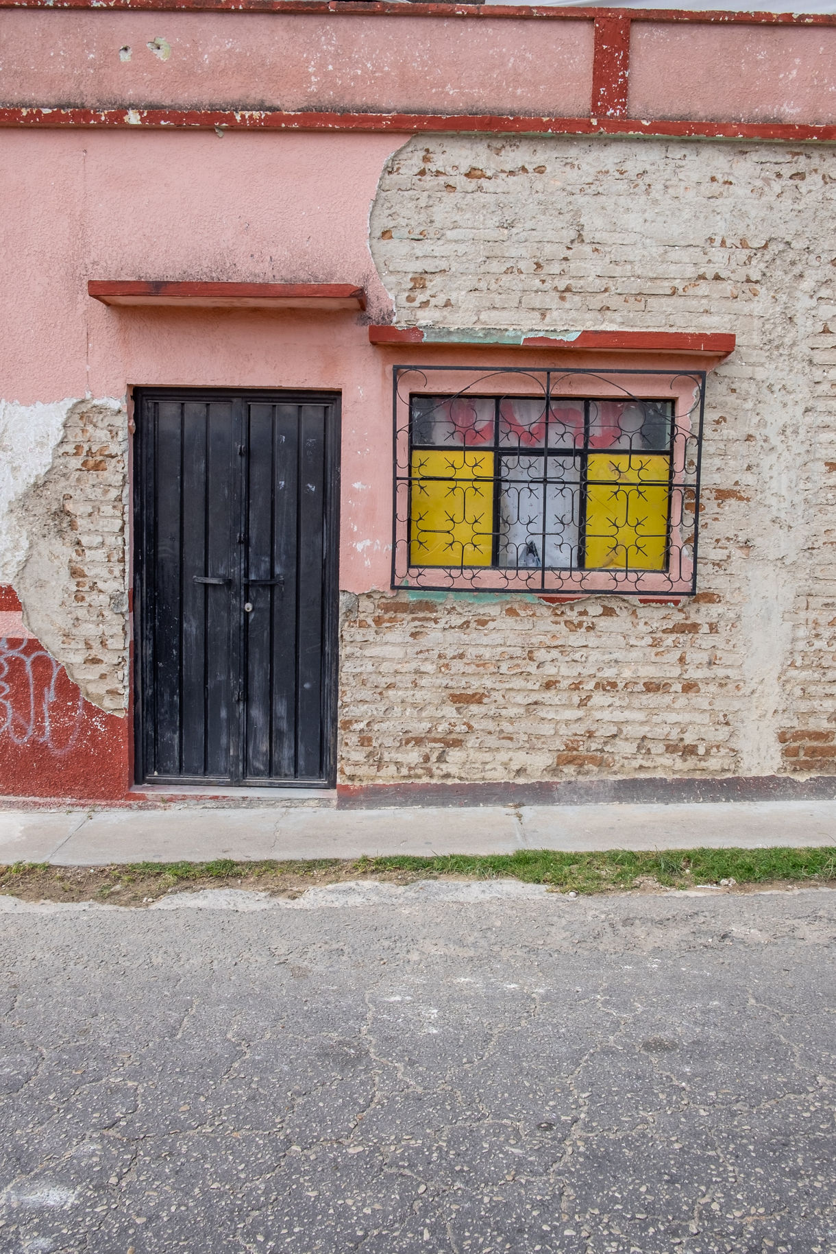 Weathered pink wall in Comitán, Chiapas, with black wooden door and window framed by yellow and red stained glass.