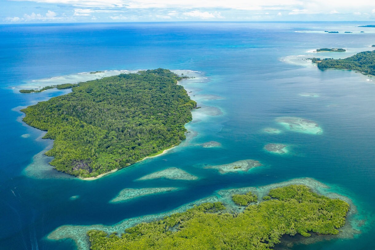 Aerial view of small tropical islands with dense green forest and bright turquoise water.