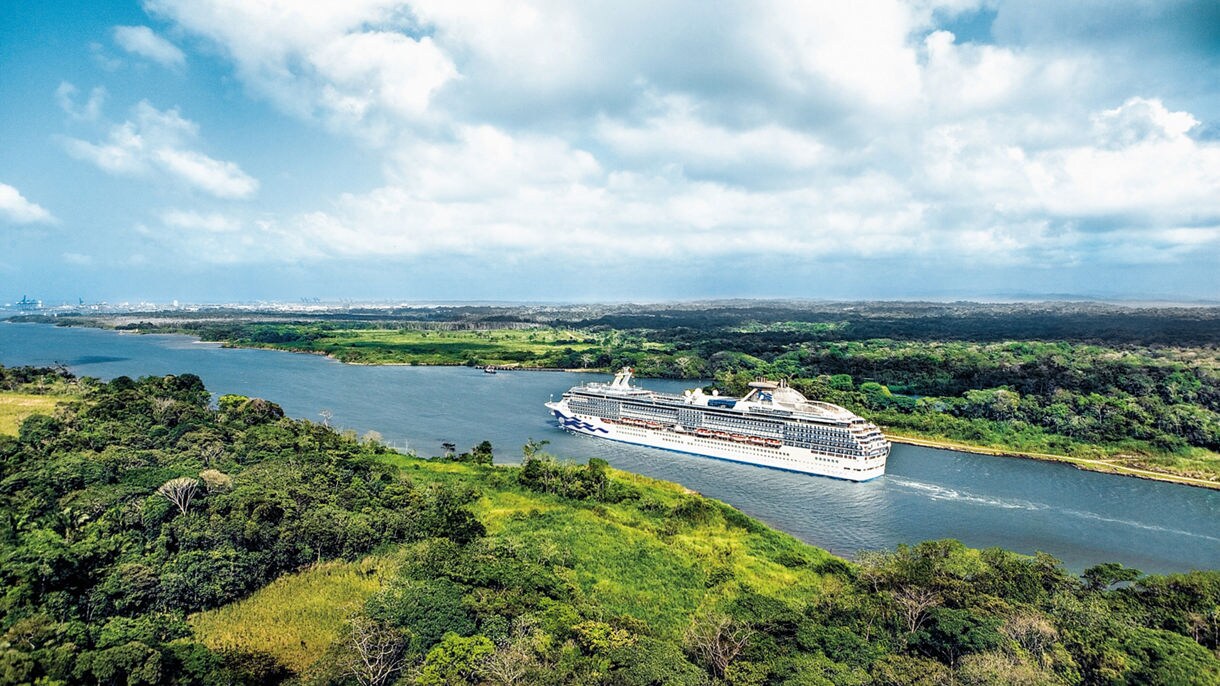 A Princess cruise ship sailing through Gatun Lake in the Panama Canal, surrounded by green forests and a wide, open sky.