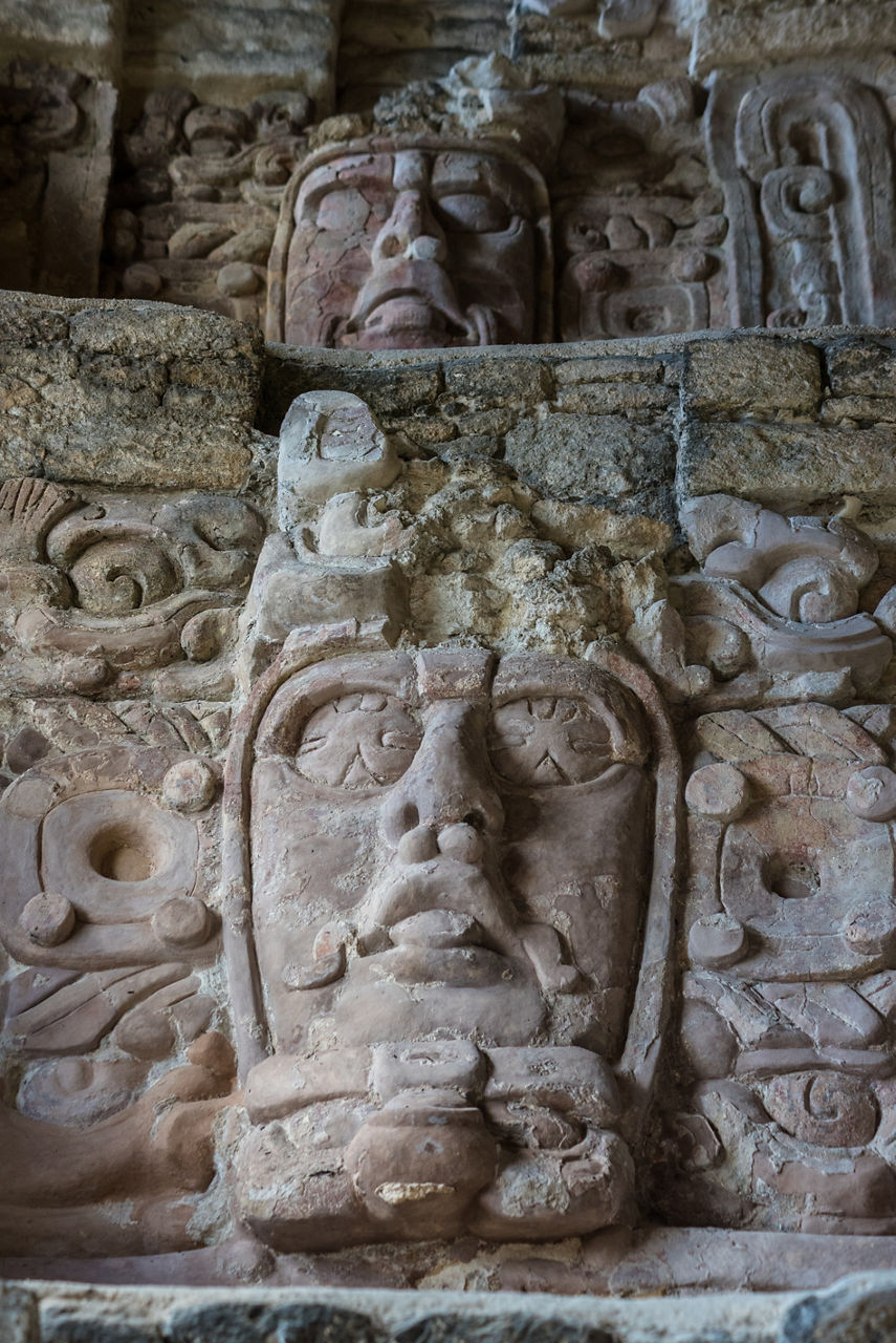 A close-up of detailed Mayan stone carvings at a temple ruin in Costa Maya featuring two large sculpted faces with intricate patterns and sacred symbols etched into the weathered stone.