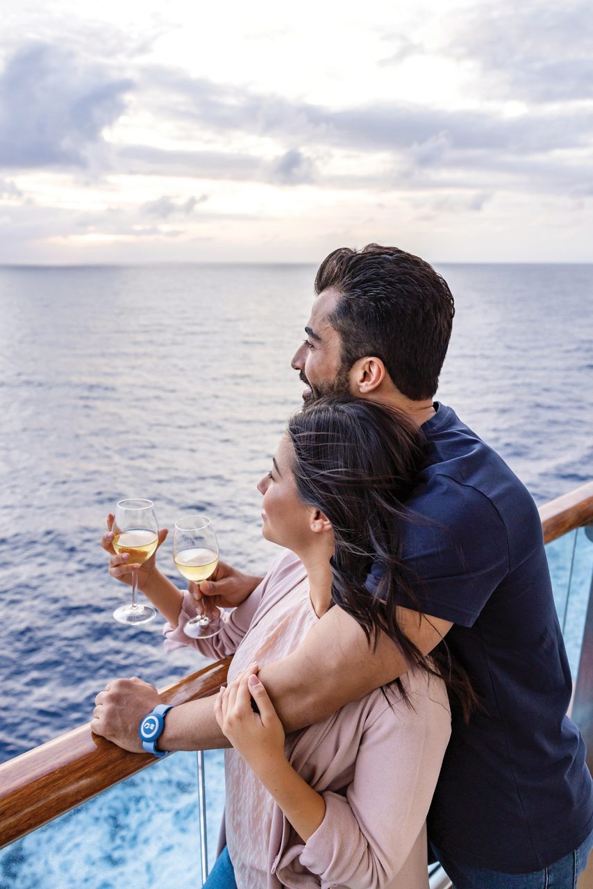 Couple holding glasses of champagne, watching the sea from the balcony