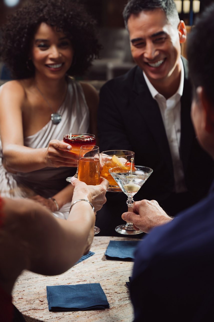 A group toasts with martinis and cocktails around a table while sharing smiles. 