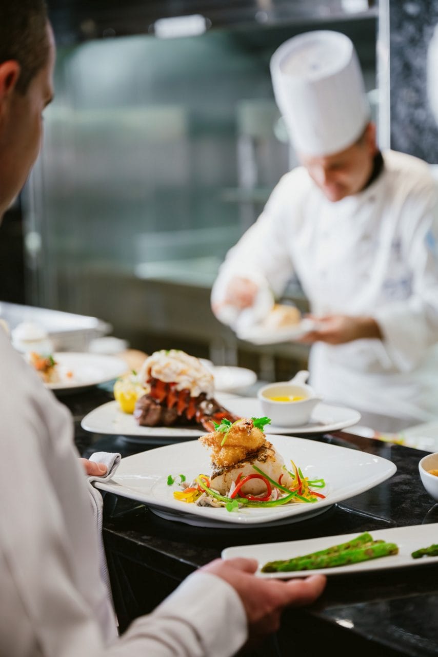 Crown Grill chefs engaged in food preparation within a vibrant restaurant kitchen, emphasizing teamwork and culinary artistry.