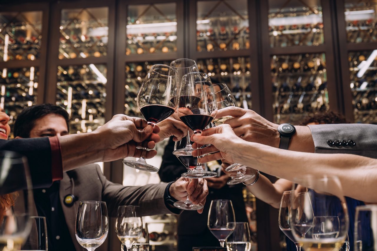 A group of elegantly dressed guests toasting with glasses of red wine at Crown Grill, enjoying a lively and sophisticated dining experience.