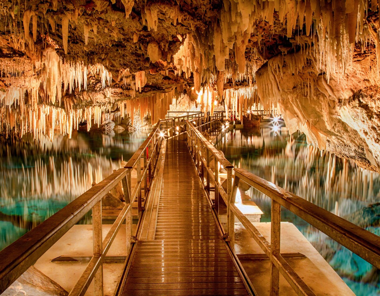 Walkway inside Bermuda’s Crystal Caves surrounded by stalactites and illuminated turquoise water.