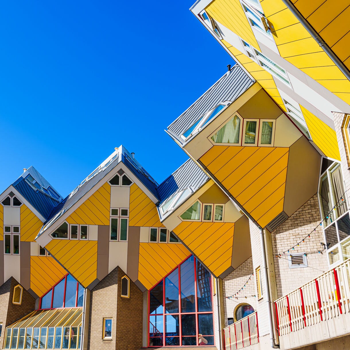 Row of Rotterdam’s Cube Houses with bright yellow panels and slanted geometric design set against a vivid blue sky.