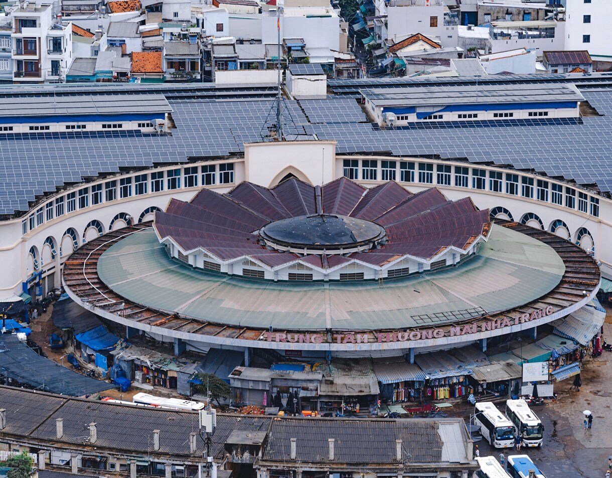 Aerial view of Dam Market in Nha Trang, Vietnam, showing its circular design with a flower-shaped roof surrounded by busy stalls and nearby buildings.
