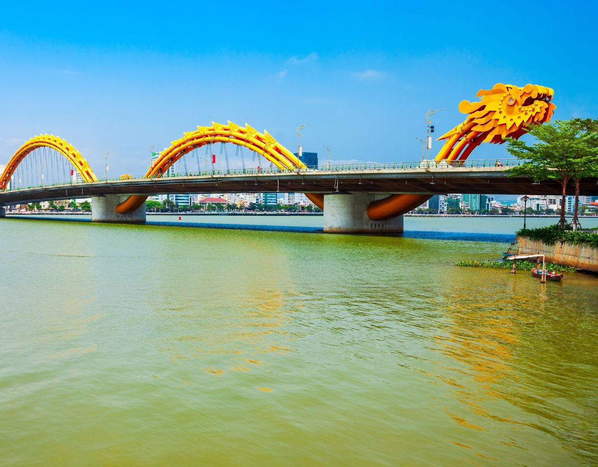 The bright yellow Dragon Bridge in Da Nang, Vietnam, spans the Han River under a clear blue sky.