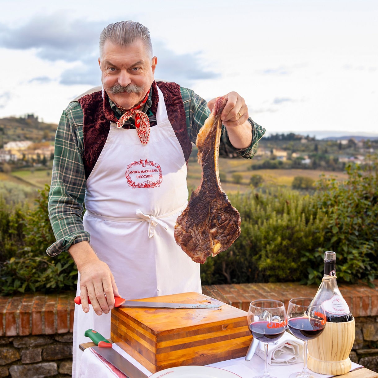 Multiple plates of sliced steaks and accompaniments arranged on a wooden table with wine glasses.