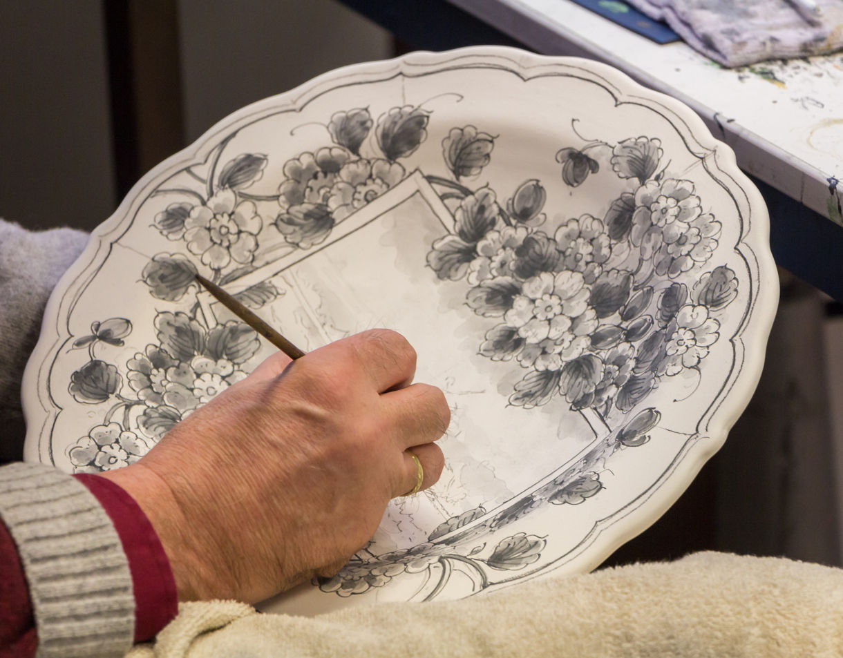 Close-up of an artisan painting floral designs on a Delft Blue ceramic plate.
