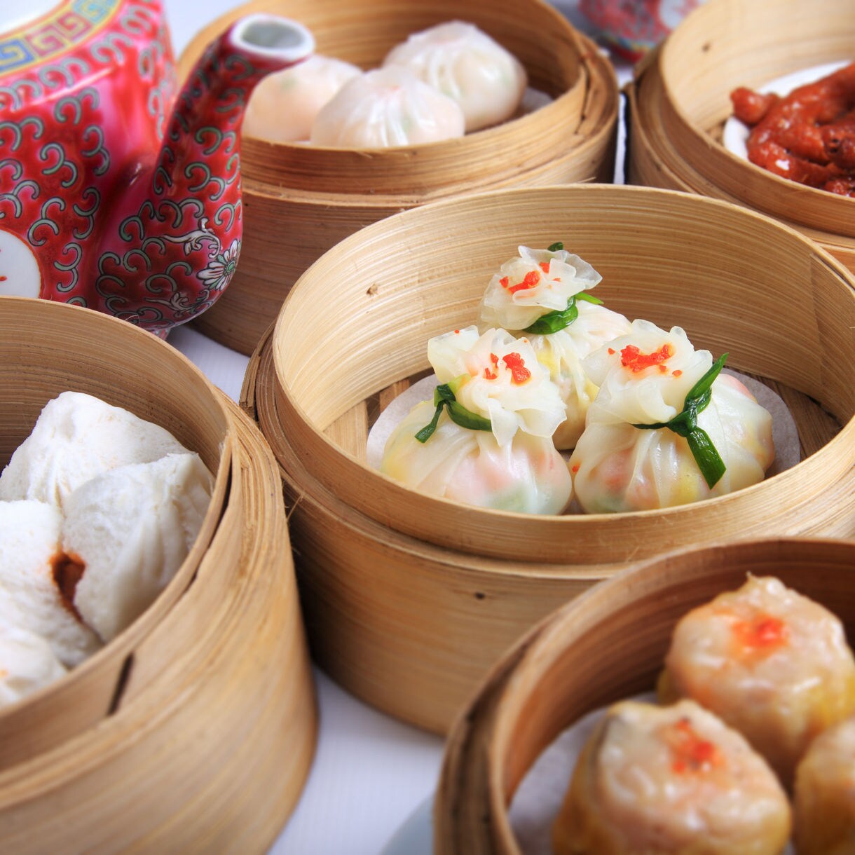 A table filled with bamboo steamers of dim sum, including dumplings, buns and a red teapot, showcasing a traditional Hong Kong meal.