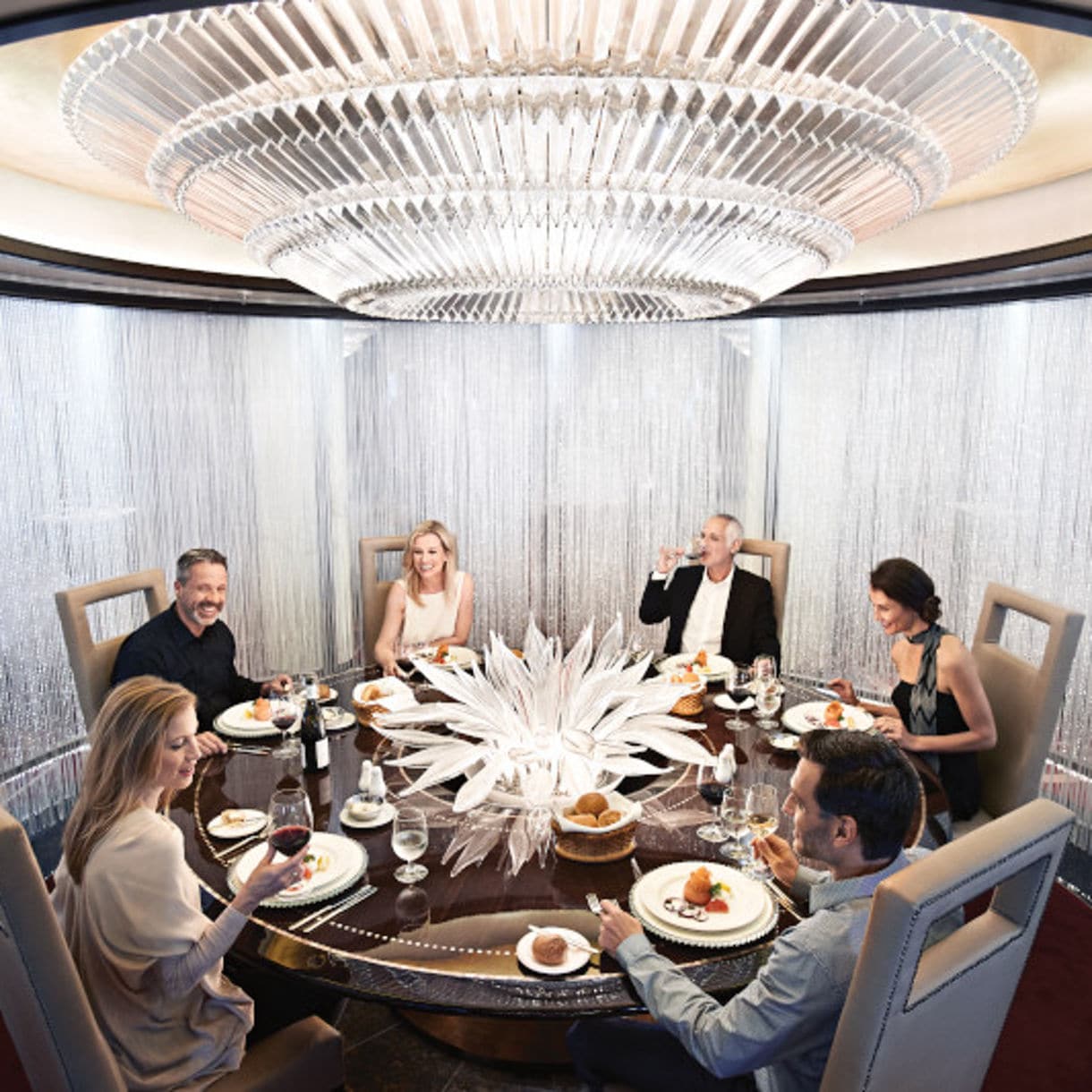 An elegant private dining room with a glass dome ceiling, featuring a round table where guests are seated for an exclusive chef's table experience.