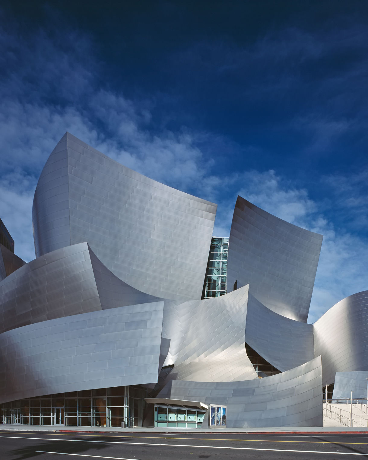 Exterior view of the Walt Disney Concert Hall showcasing its dramatic stainless-steel panels set against a bright blue sky with light clouds.