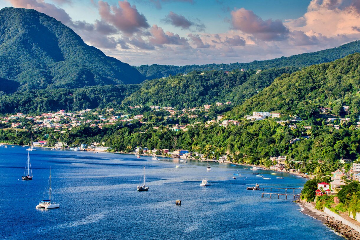 Aerial view of Roseau, Dominica's capital, showing colorful buildings, a waterfront with a pier and the lush mountains surrounding the city.