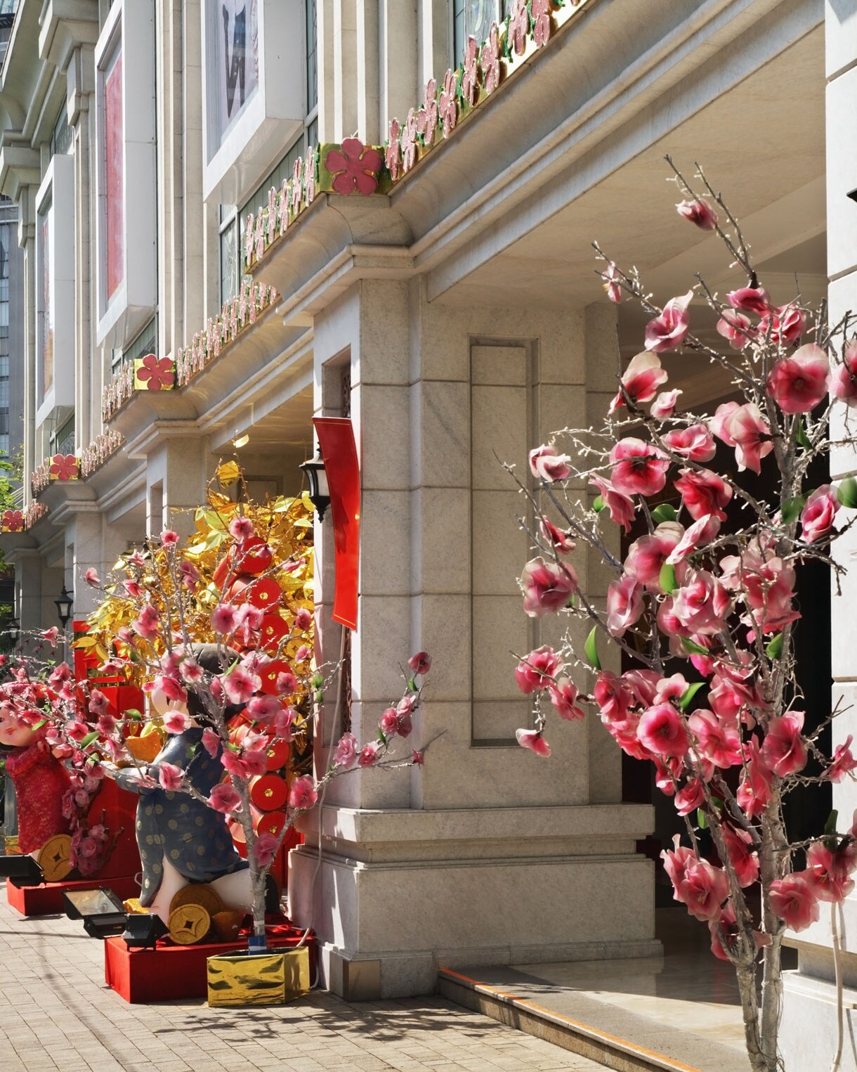 Pink cherry blossom decorations along the marble storefronts of Dong Khoi Street in Ho Chi Minh City, glowing under bright afternoon sun.