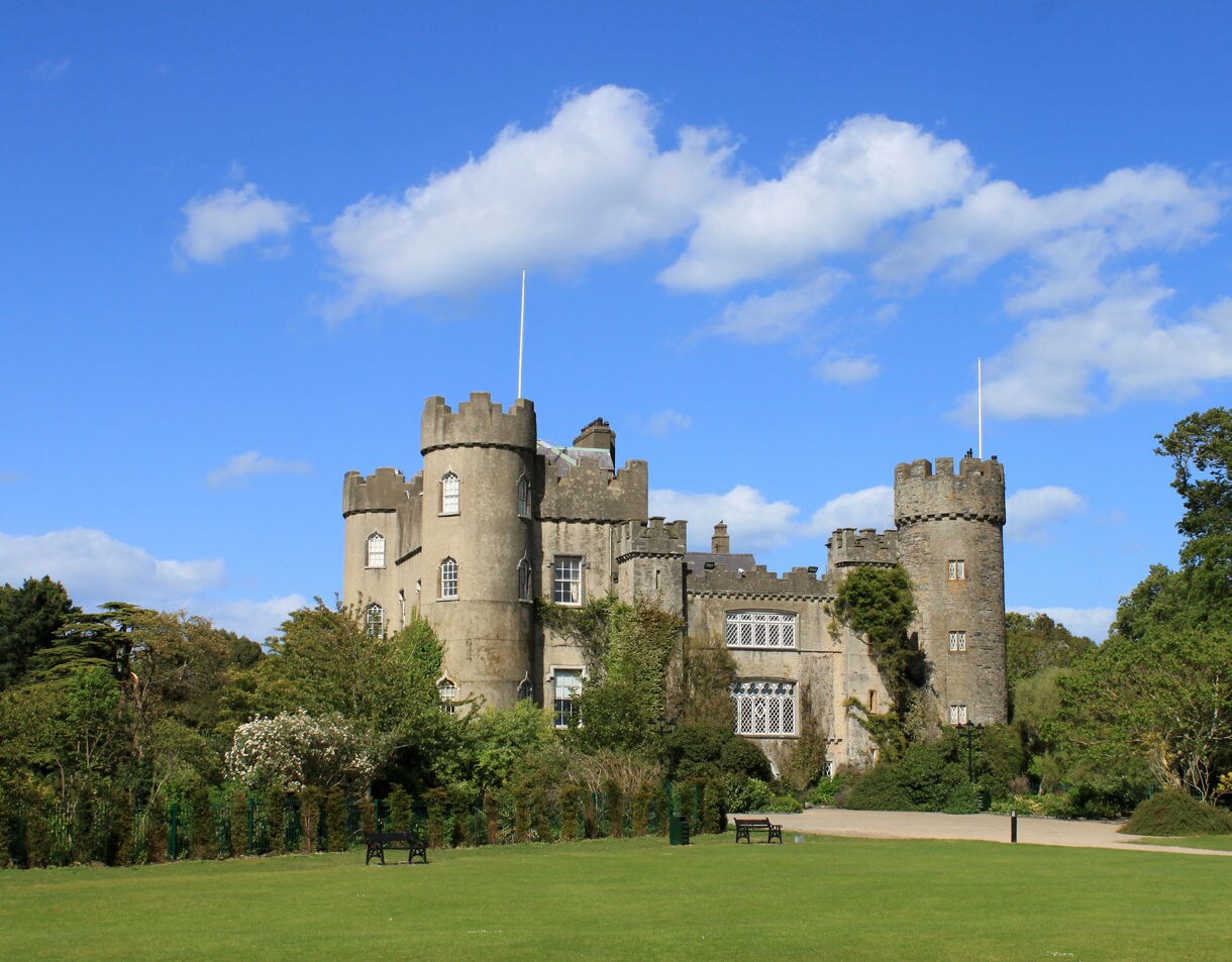 Malahide Castle in Dublin, with ivy-clad stone towers surrounded by gardens and open green lawns.
