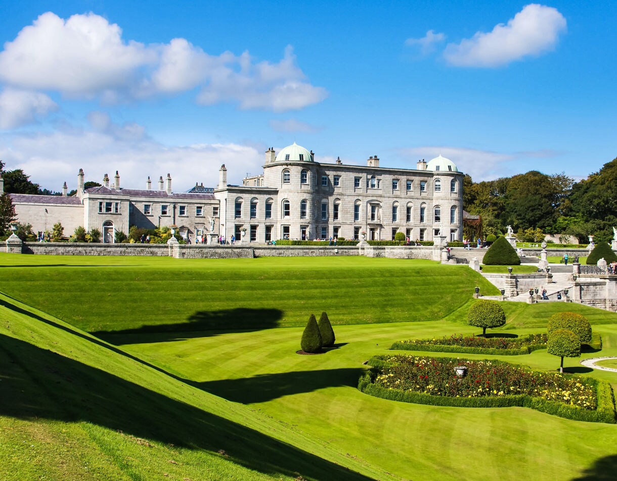 Powerscourt Estate near Dublin with manicured lawns, sculpted hedges and a stately mansion under a bright blue sky.