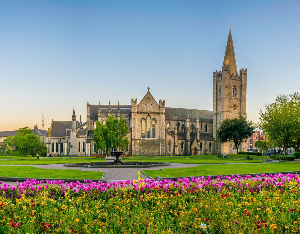 St. Patrick’s Cathedral in Dublin at sunset, framed by colorful tulip-filled gardens and lush green lawns.