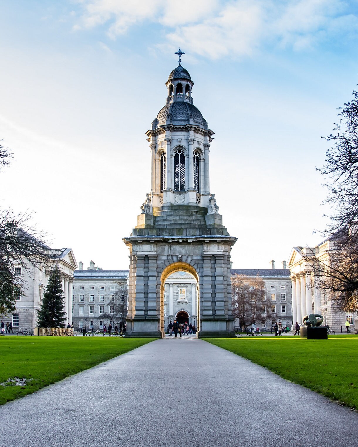 Trinity College Dublin with its grand bell tower centered between historic stone buildings and green lawns.