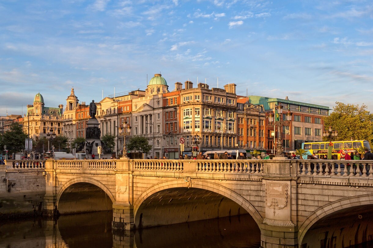 O’Connell Bridge in Dublin at golden hour, with historic buildings and a yellow double-decker bus lining the riverside.