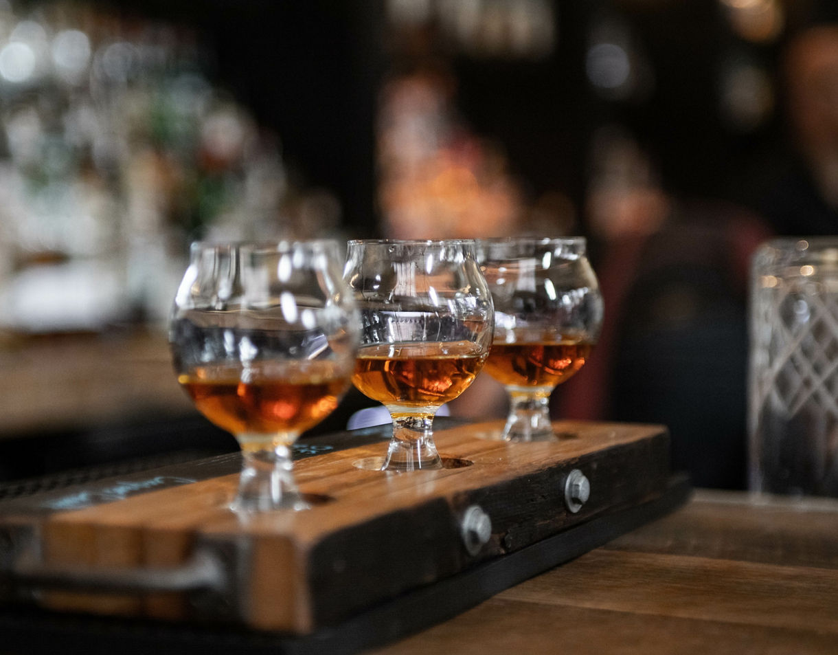 Three glasses of golden Irish whiskey served on a wooden tasting tray inside a bar.