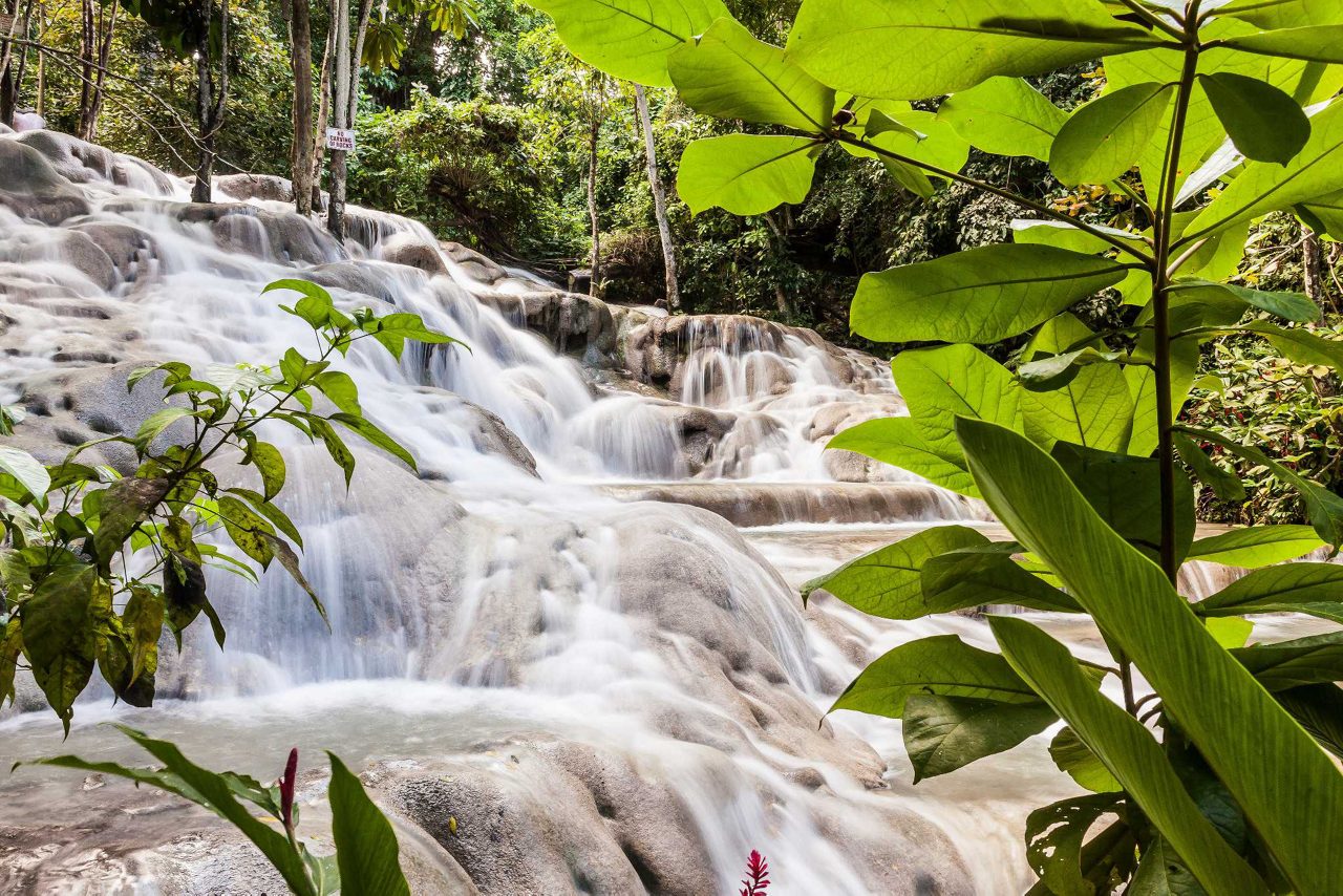 Dunn’s River Falls in Jamaica featuring terraced limestone rock formations, clear rushing water and dense green foliage with visitors climbing the waterfall.
