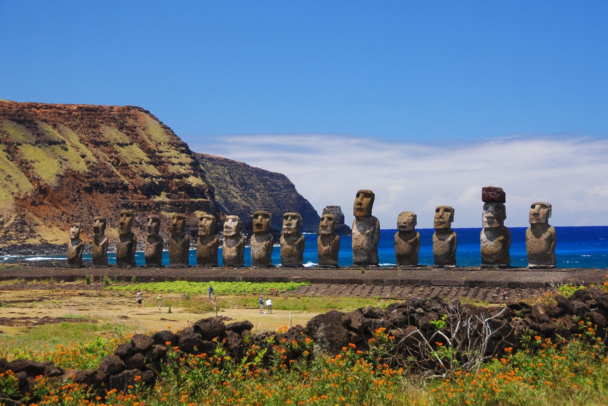 Long row of restored moai statues at Ahu Tongariki on Easter Island, set against blue ocean and rugged coastal cliffs.