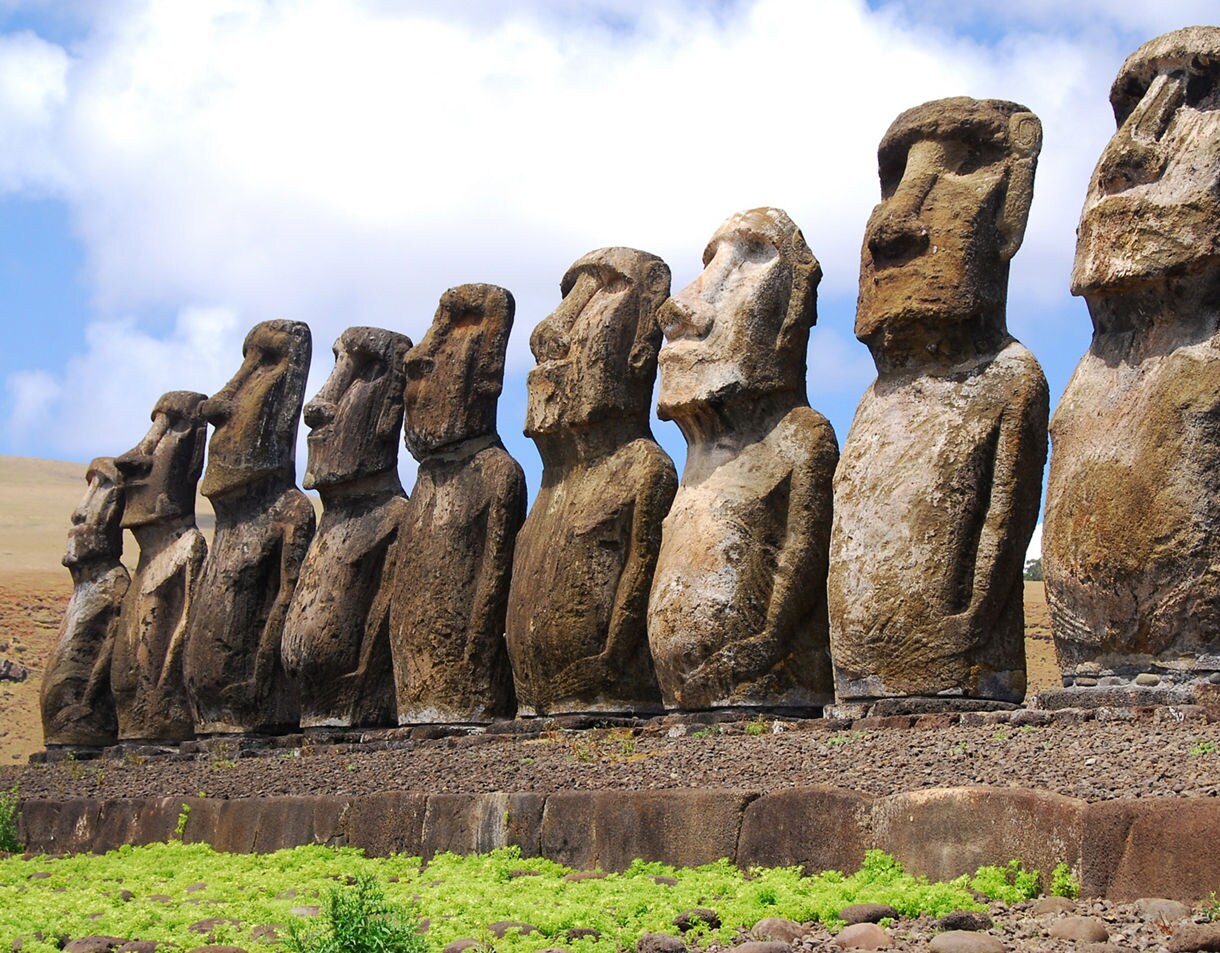 Row of towering moai statues on Easter Island standing on a stone platform under a partly cloudy sky.