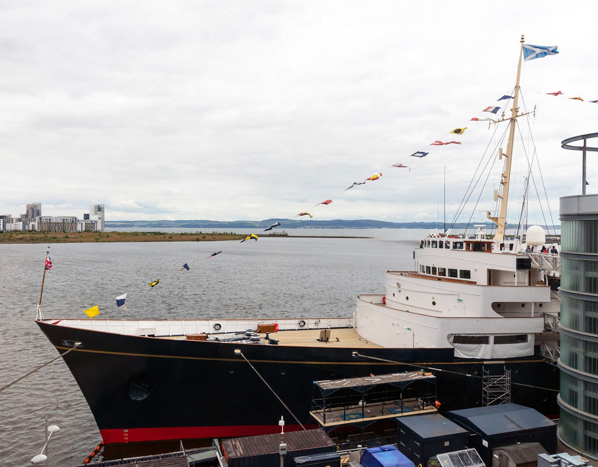 The Royal Yacht Britannia docked in Edinburgh, decorated with colorful signal flags and a Scottish flag flying from the mast.