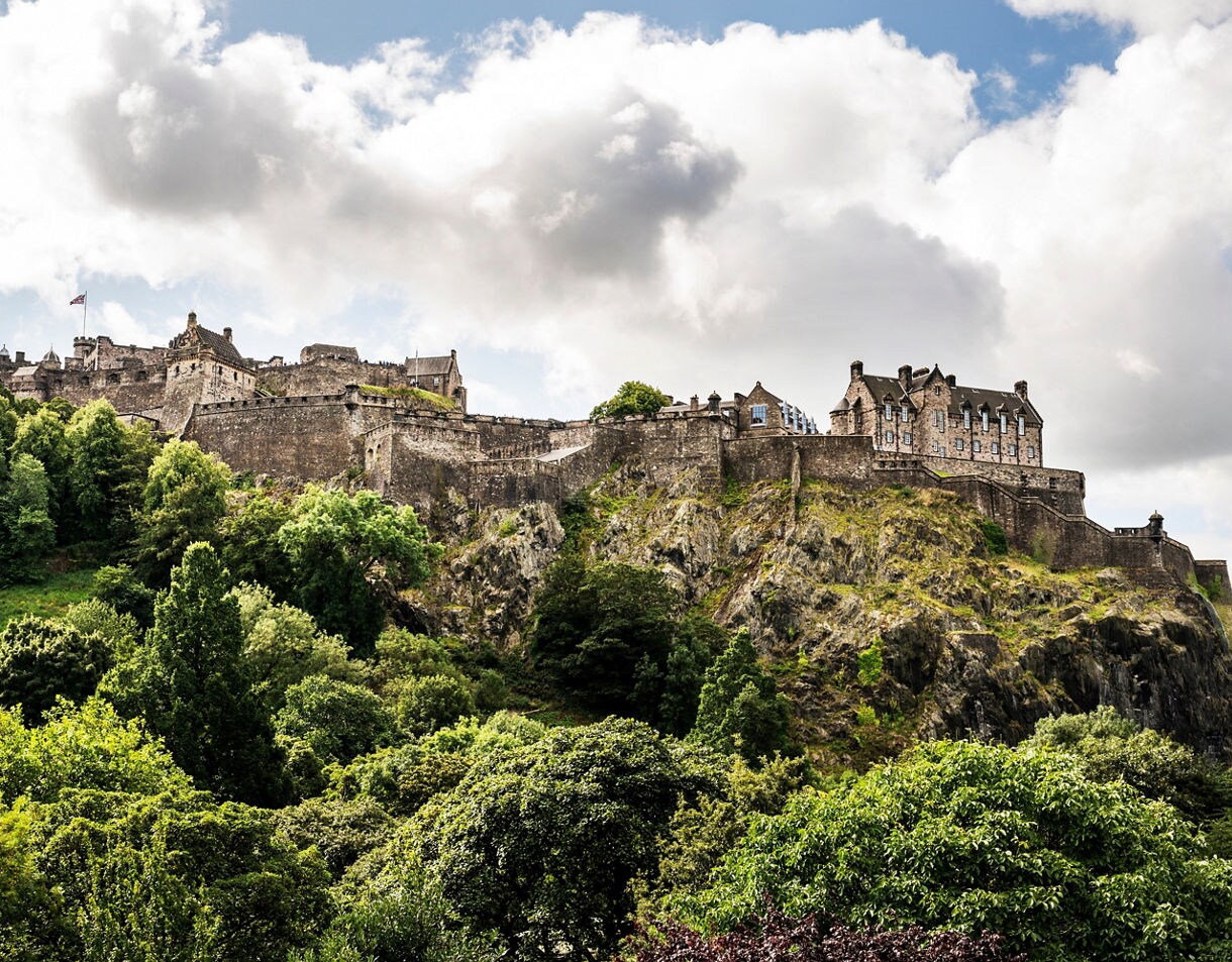 Edinburgh Castle perched on a volcanic rock with stone walls rising above green trees.