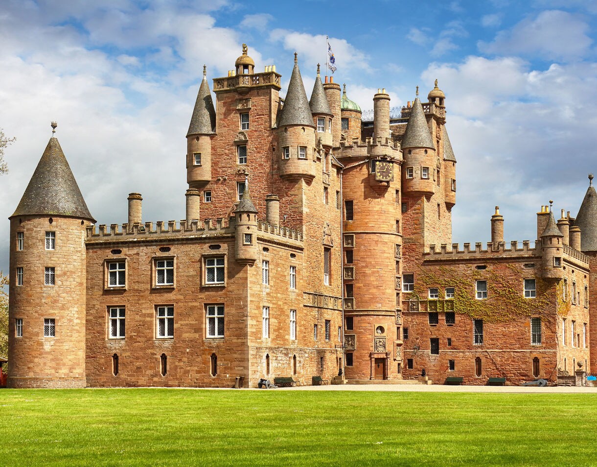 Glamis Castle in Scotland featuring red sandstone walls, turrets and a wide green lawn.