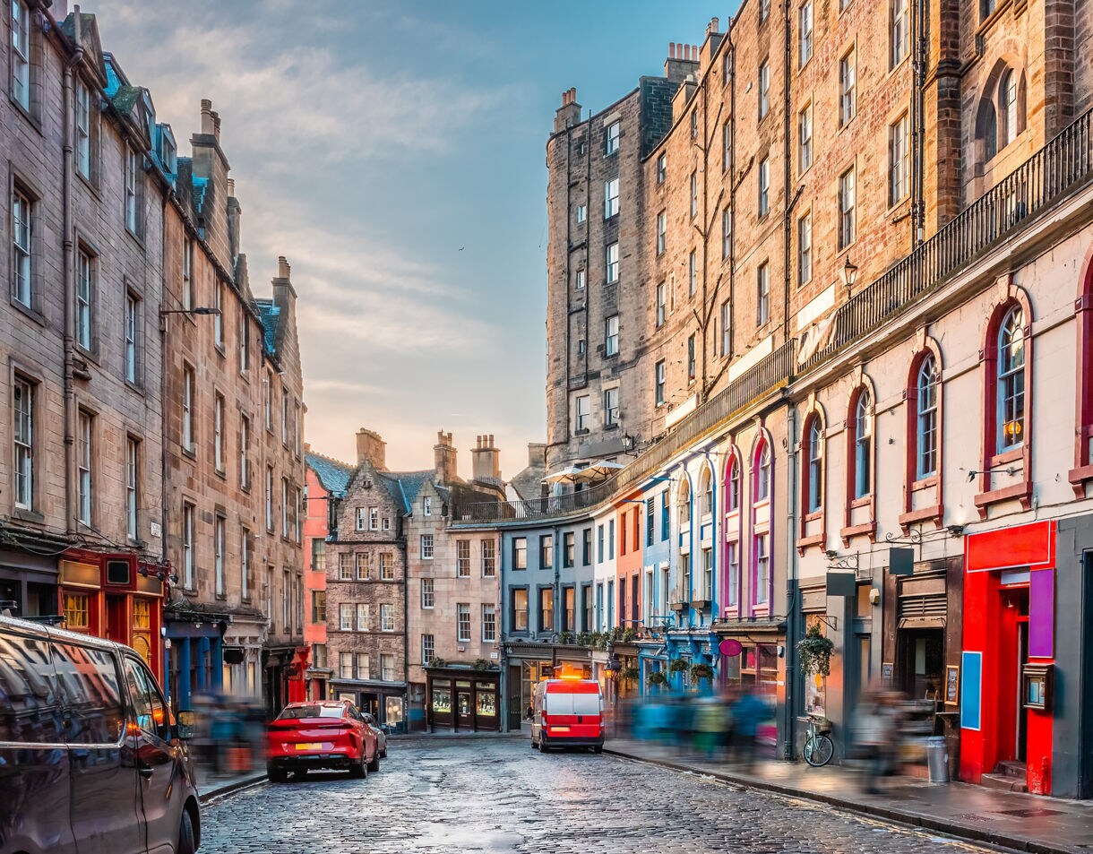 Curved street in Edinburgh with tall stone buildings and brightly painted storefronts.