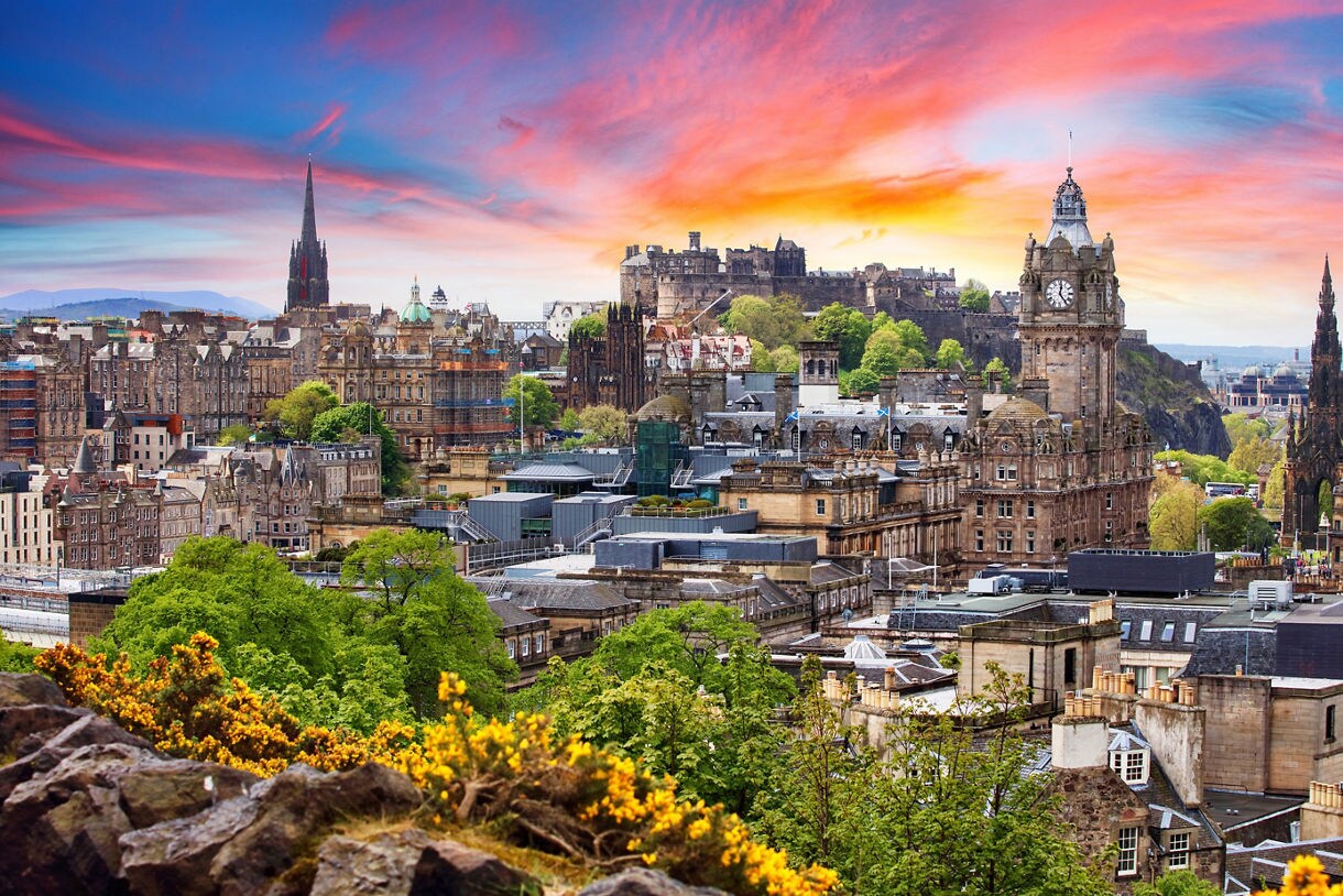 View of Edinburgh’s historic skyline with the castle, clock tower and spires at sunset.
