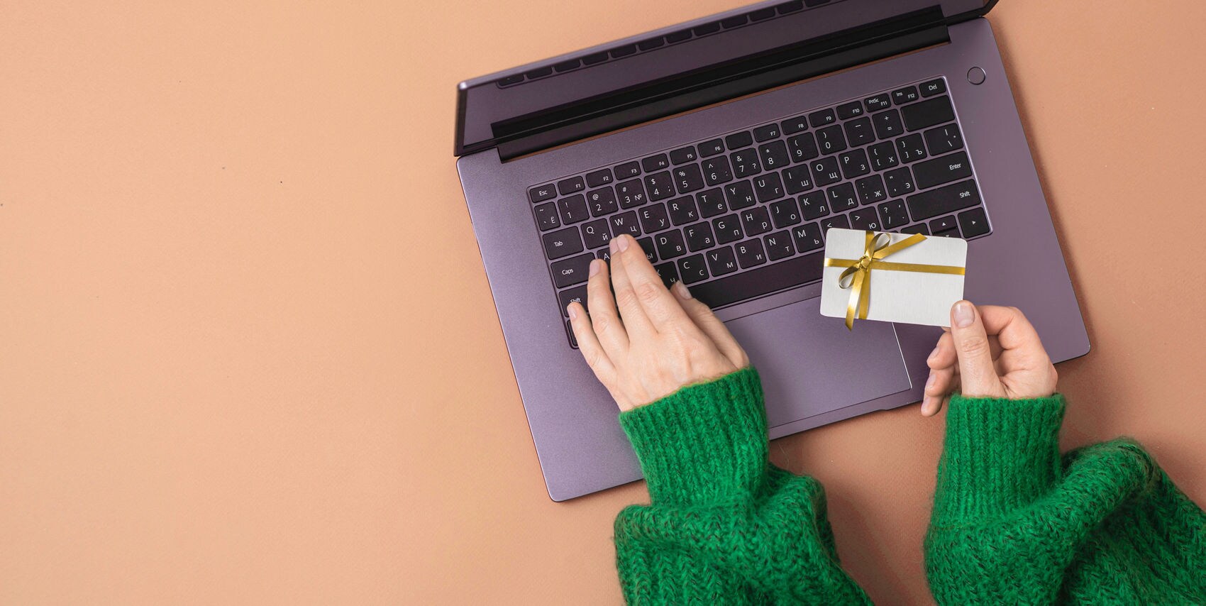 A person holds a gift card while using a laptop, illustrating how easy it is to buy and send a Princess Cruises eGift Card online.