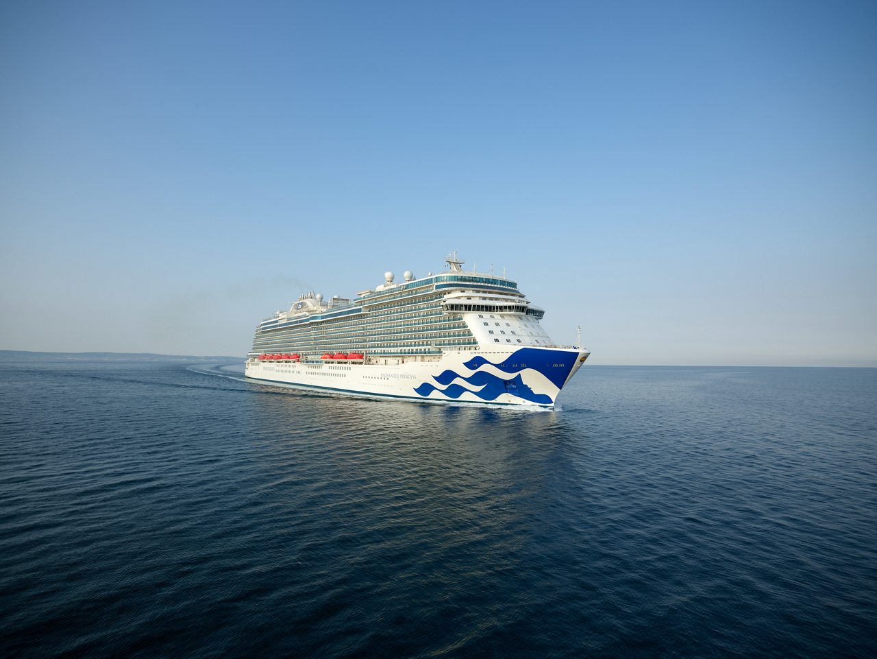  A large Princess Cruises ship, the Enchanted Princess, cruising across a serene ocean under a clear blue sky. 