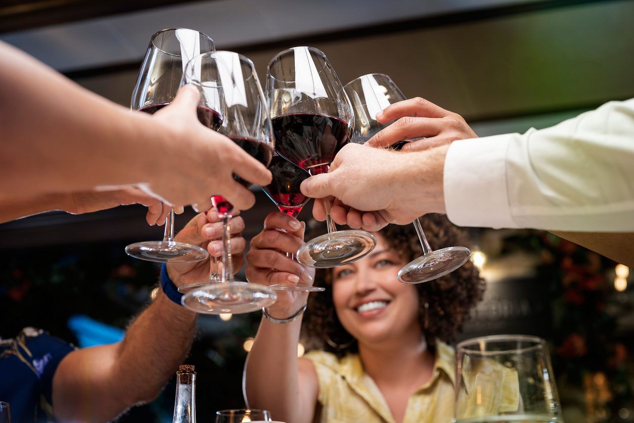  Multiple hands raising wine glasses in a celebratory toast at Sabatini's Italian Trattoria, with smiling guests visible in the background.