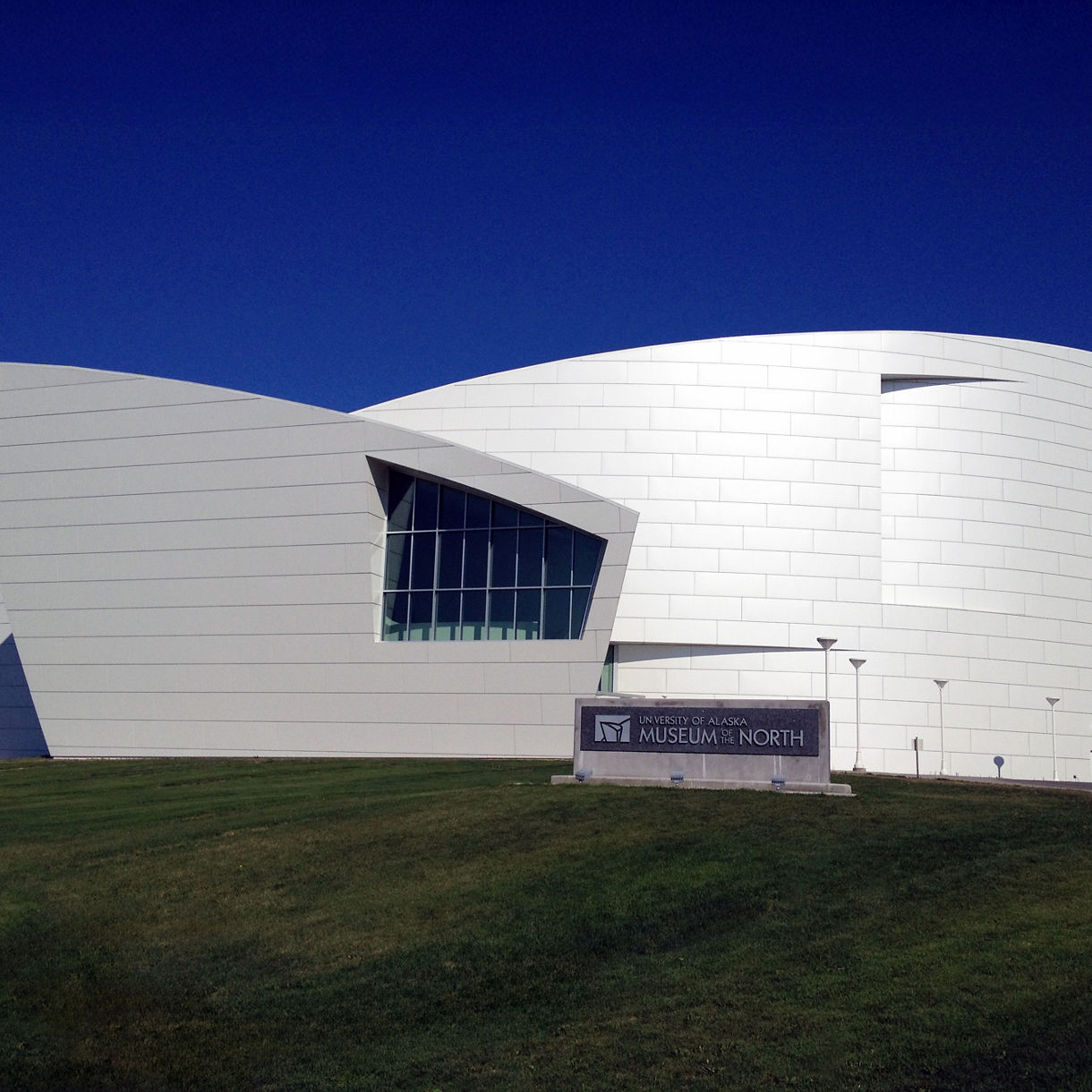 The University of Alaska Museum of the North in Fairbanks, featuring a bold, angular white facade with curved and geometric lines set against a clear blue sky.