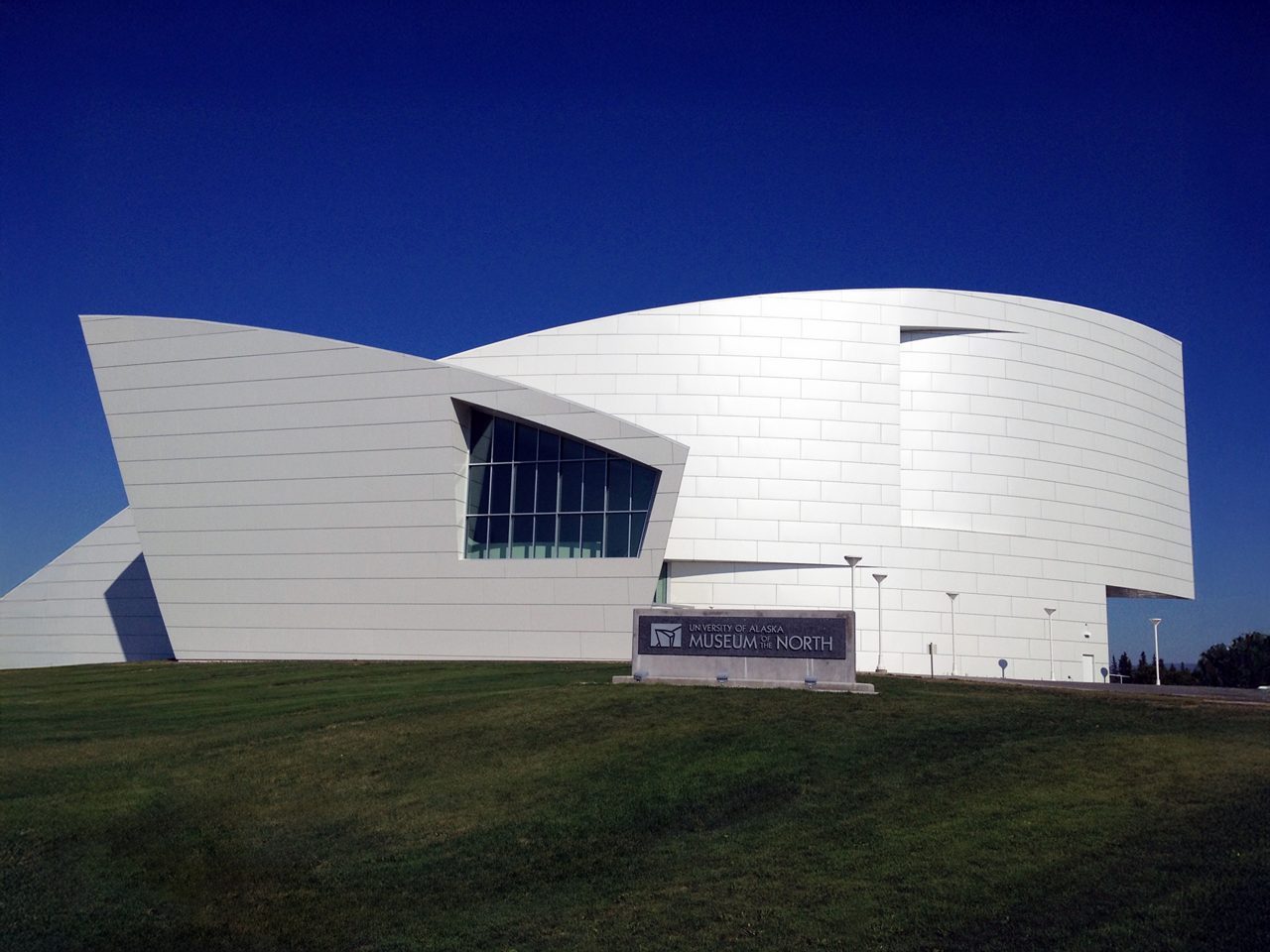The University of Alaska Museum of the North in Fairbanks, featuring a bold, angular white facade with curved and geometric lines set against a clear blue sky.