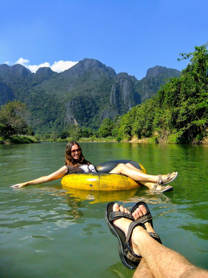 A woman relaxing in a yellow inner tube on a calm jungle river with lush green trees and tall mountains in the background.