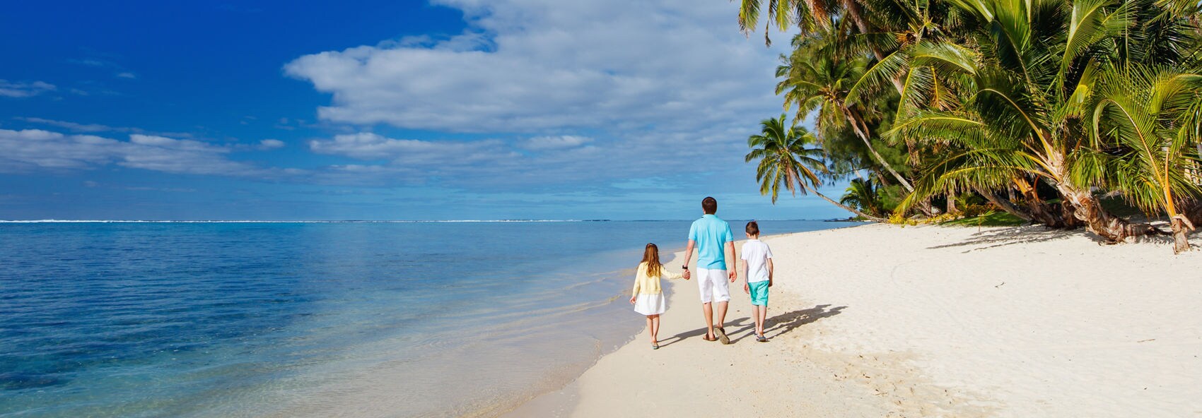 A joyful couple walking along a beach at the edge of clear turquoise water. They appear to be laughing and enjoying their time together in a tropical setting. The beach scene is calm, with the horizon visible under a cloudy sky.