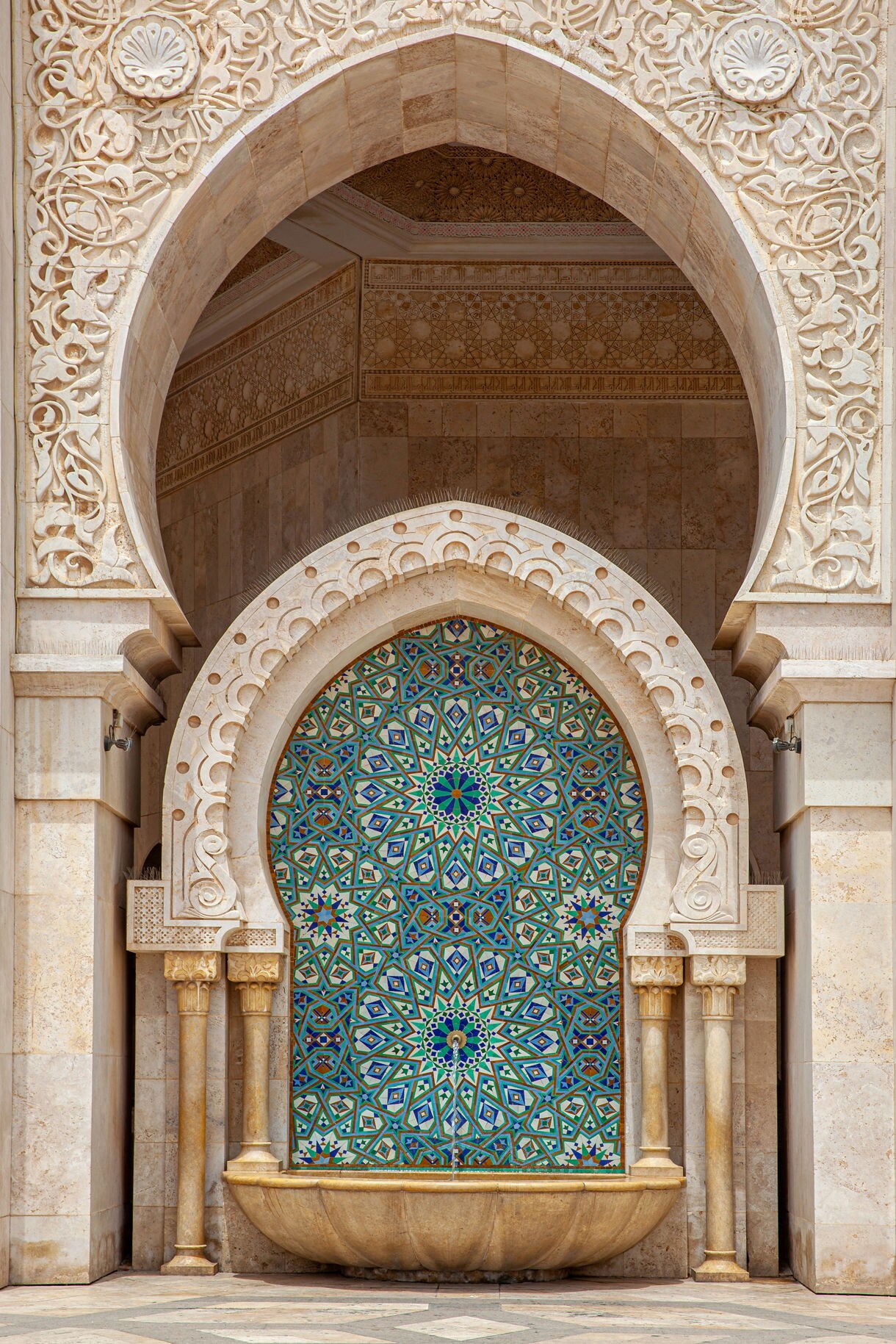 Ornate geometric tile fountain set within carved stone arches.