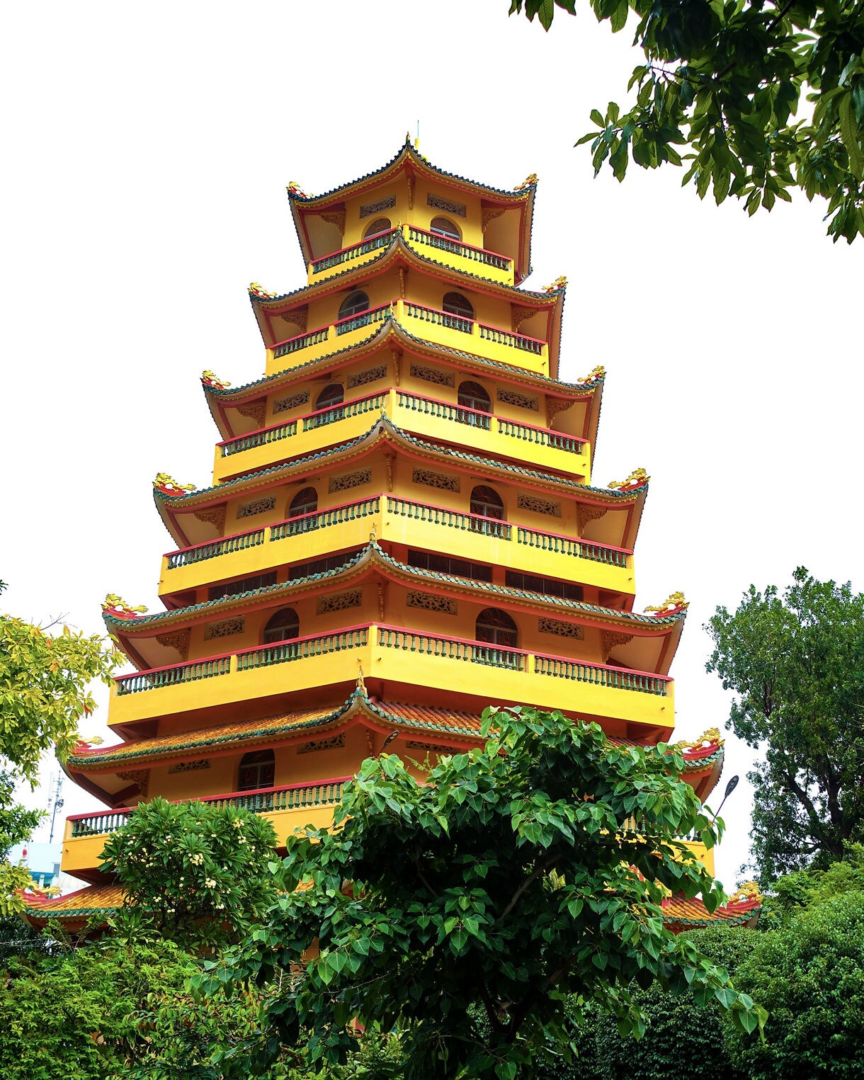 Tall yellow multi-tiered pagoda with ornate green and red roofs surrounded by trees and greenery at Giac Lam Pagoda.