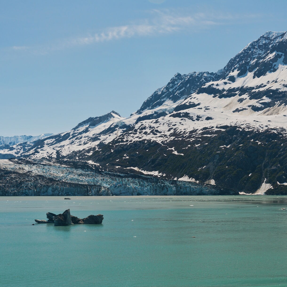 View of Johns Hopkins Inlet in Glacier Bay National Park with floating icebergs and a glacier descending from snow-capped mountains into the turquoise water below.