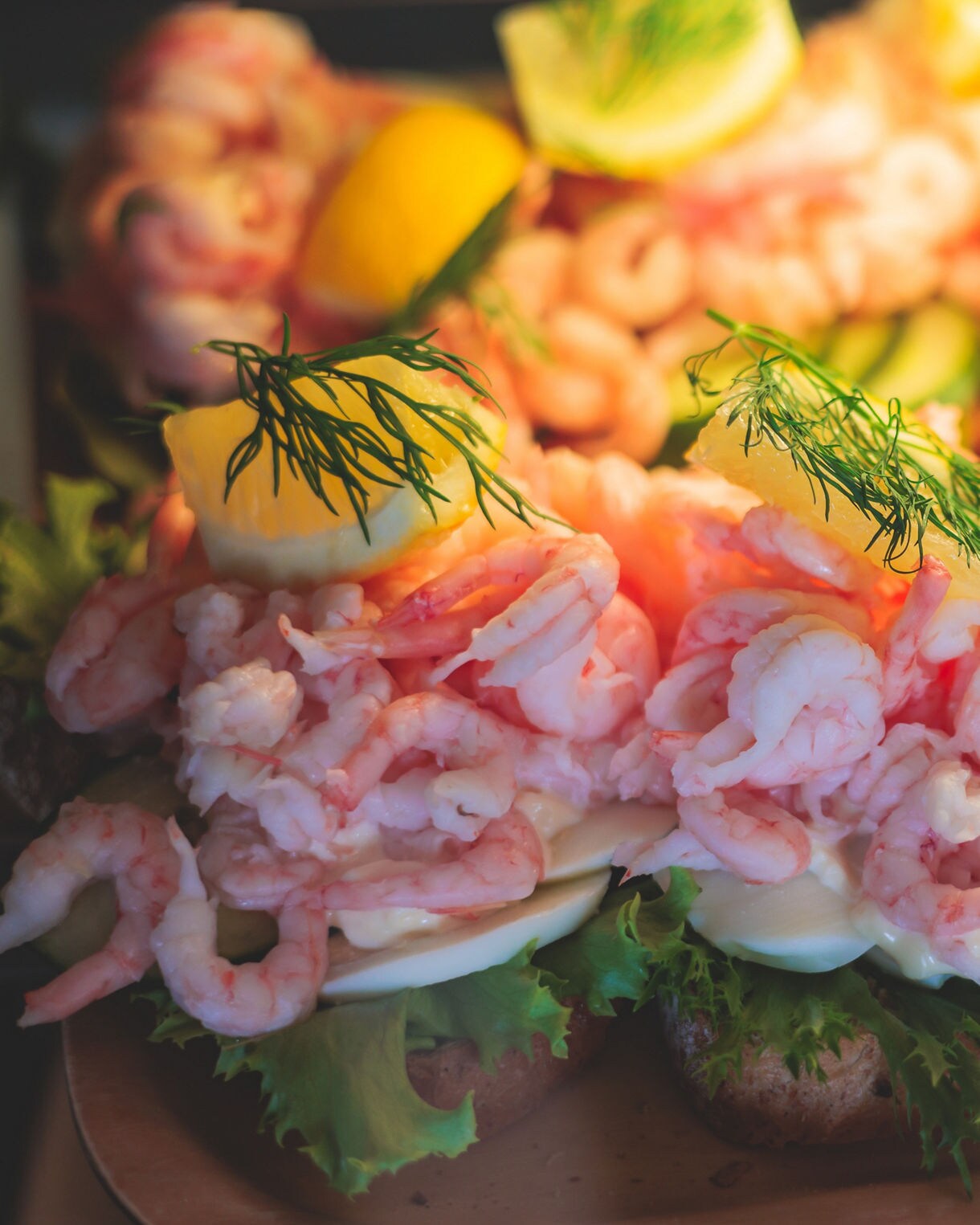 A close-up view displays open-faced Swedish shrimp sandwiches heavily topped with small pink cold-water shrimp, fresh dill sprigs, and lemon wedges.