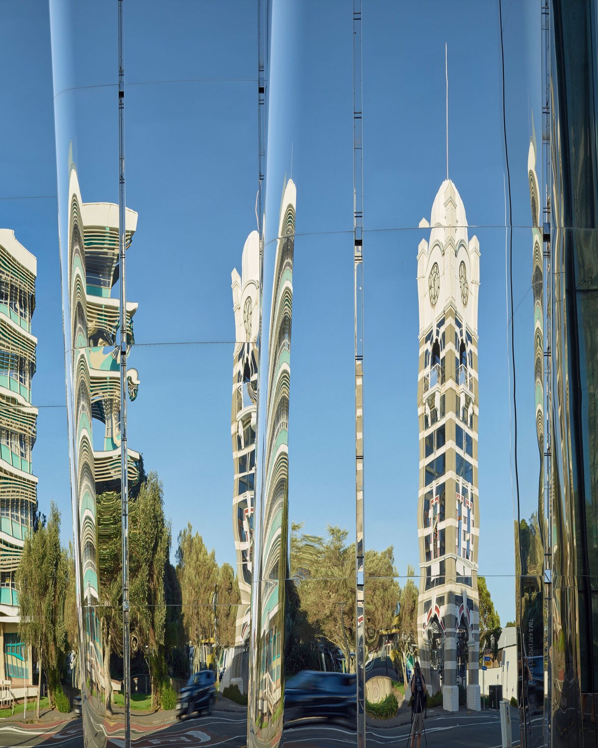 Reflections of nearby buildings and a clock tower distorted in the polished, curved stainless steel exterior of the Len Lye Centre in New Plymouth.